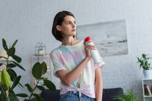 Woman spraying air freshener near plants at home